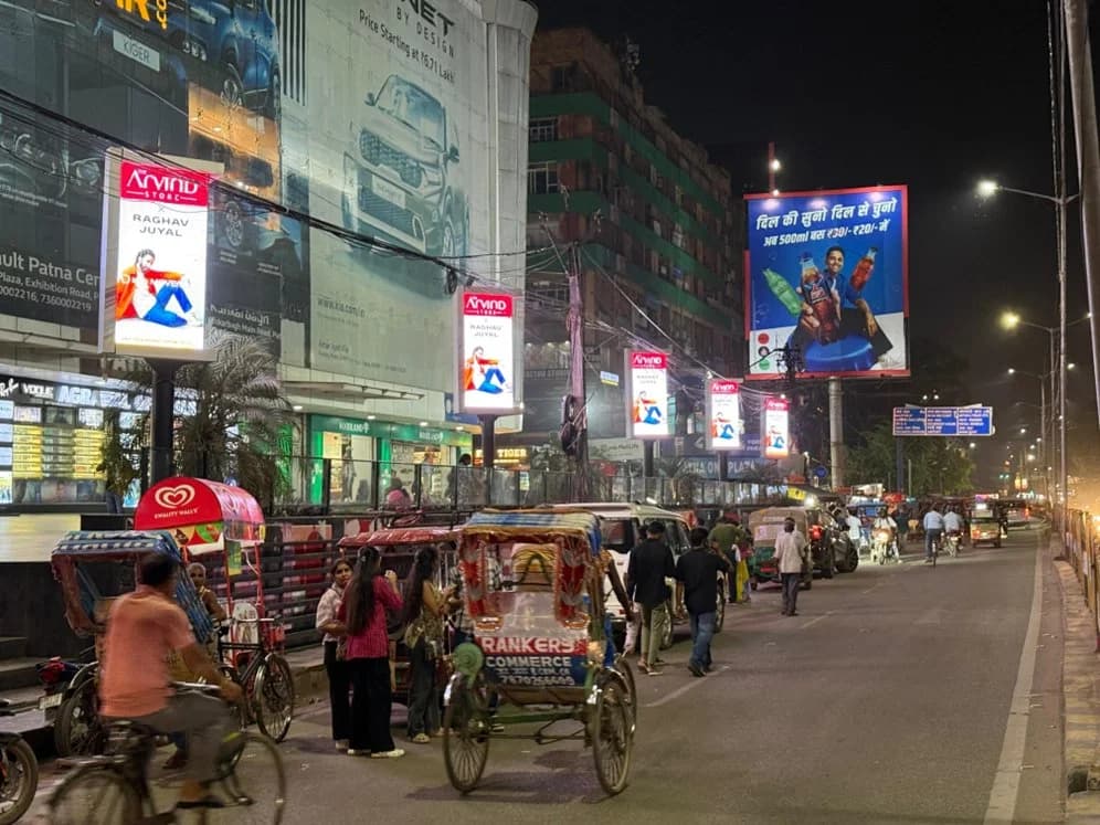 Street lined with illuminated pole kiosks and a large hoarding at night, Patna
